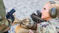 Eine US-Soldatin liegt hinter einem Sandsack mit Maschinenpistole und hört einem deutschen Soldaten zu