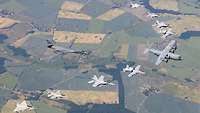Am Himmel sind acht Kampflugzeuge zu sehen, die ein Bomben- und ein Transportflugzeug begleiten