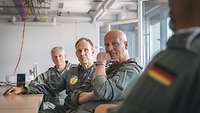 Three high-ranking soldiers in flight suits are sitting in a conference room.