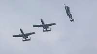 Three A-10 jets fly in the air as a formation. One of them breaks away to the left.