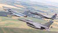 Three fighter jets fly in formation over agricultural land.