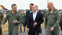 Two soldiers and Olaf Scholz walk side by side.