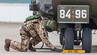 A soldier pushes a block of wood in front of the tires of a stationary aircraft.