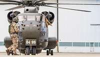 A CH-53 stands on the Lechfeld. A soldier is walking around in front of it.