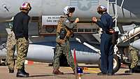 Two soldiers bump fists in greeting in front of an airplane.