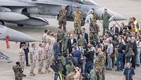 A crowd of media representatives surrounds Chancellor Olaf Scholz in front of fighter jets.