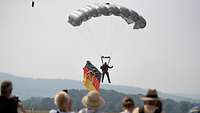 Ein Fallschirmspringer landet auf einer Freifläche mit einer Deutschlandflagge