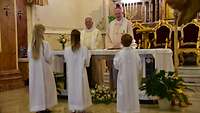 Der Katholische Militärbischof Franz-Josef Overbeck erteilt die Erste Heilige Kommunion an drei Kinder