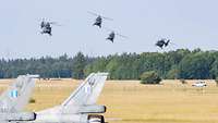 Four H145M helicopters fly over a field.