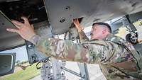 An American soldier checks something on the lower fuselage of an aircraft.