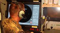 Ein Soldat sitzt mit Kopfhörern vor einem Bildschirm in einem Flugabwehrraketen-System "Patriot".