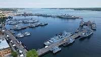 Luftbild eines Hafens, in dem viele graue Kriegsschiffe liegen.