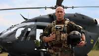 A soldier is standing in front of a helicopter on the taxiway.