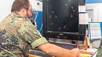 An air traffic controller is sitting at a radar screen and communicates with an aircraft via radio.