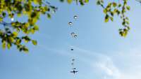 Aus einem Flugzeug am Himmel springen nacheinander Soldaten. Ihre Fallschirme sind zu sehen.