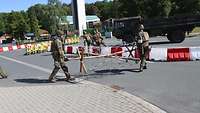 Zwei Soldaten schleppen ein Holzgestell mit Stacheldraht auf eine Fahrbahn.