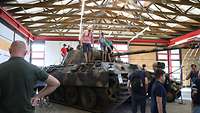In einer Halle klettern Zivilisten auf einem Kampfpanzer herum.