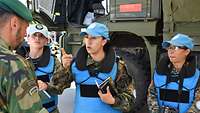 Drei Militärbeobachterinnen in hellblauen Schutzwesten sprechen mit einem Darsteller.