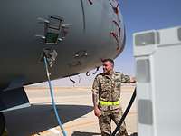 Ein Soldat steht vor einem Flugzeug, an dem ein Wasserschlauch angebracht ist. 