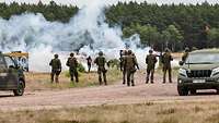 Eine Gruppe von Soldaten steht vor einer Reihe Demonstranten die Rachtöpfe gezündet haben.