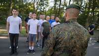 Junge Menschen stehen im Hintergrund, vor Ihnen ein Soldat