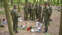 Soldaten stehen in einer Gruppe vor einem Ausbilder im Wald 