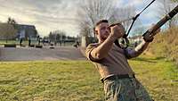 Ein Soldat trainiert am TRX Schlingentrainer auf einer Wiese im Freien.