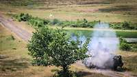 Ein Schützenpanzer steht neben einem Baum und hat gerade eine Rakete abgefeuert.