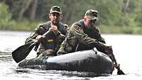 Es regnet: Zwei Soldaten mit Paddel in der Hand überqueren im Schlauchboot einen Fluss.