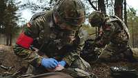 Zwei Sanitäter knienn im Wald bei einem Verletzten.