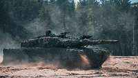 Ein Kampfpanzer Leopard fährt über sandigen Boden auf dem Übungsplatz und wirbelt dabei Staub auf.