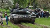 Der Kampfpanzer Leopard 2 wird im Gelände von einer Gruppe Menschen bestaunt.
