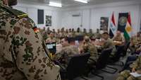 Ein deutscher Soldat bei einem Meeting. In dem Raum sitzen Soldatinnen und Soldaten weiterer Nationen.