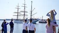 Soldaten und Zivilisten stehen am Ufer und schauen auf die einlaufende Gorch Fock