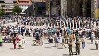 Militärmusiker spielen vor vielen Menschen auf einem Platz vor einer großen Kirche.