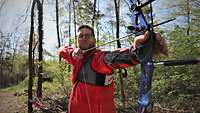 Ein Soldat mit gespanntem Sportbogen steht im Wald