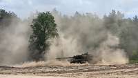 Ein Kampfpanzer fährt auf Sand und wirbelt viel Staub auf.