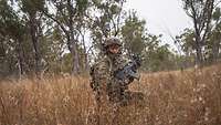 Ein Soldat mit Gewehr kniet im hohen hellbraunen Gestrüpp im Outback Australiens.