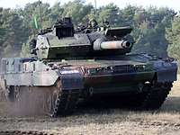 A main battle tank crosses a clearing, raising gray dust.