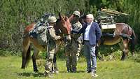 Zwei Soldaten und der Bundespräsident stehen um einen Muli.