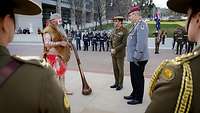 Zwei Soldaten stehen einem Ureinwohner Australiens gegenüber. Im Hintergrund stehen Soldaten.