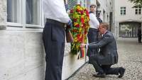 Minister Pistorius kniet vor einem Blumenkranz an der Gedenktafel im Ehrenhof des Bendlerblocks