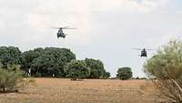 Zwei Hubschrauber fliegen etwas versetzt im Tiefflug über der spanischen Landschaft.