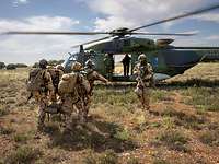 Vier Soldaten tragen eine verwundete Person auf einer Trage zum Hubschrauber. Weitere Soldaten sichern die Umgebung. 