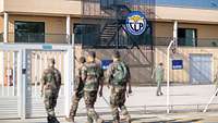 Vier Soldaten bewegen sich auf das Eingangstor zum Trainingsgelände der Air Base zu, das im Hintergrund abgebildet ist. 