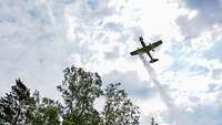 Ein Flugzeug fliegt über Bäume und wirft eine Flüssigkeit ab.