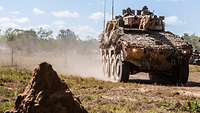 Ein Radpanzer fährt über einen rotbraunen Sandweg im australischen Outback.