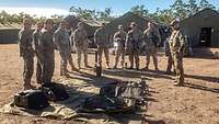 Soldaten in unterschiedlichen Uniformen stehen im Halbkreis um eine Plane, auf ihr technische Geräte