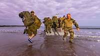 Soldaten laufen durch seichtes Wasser zu einer Fähre am Strand.