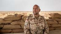 Ein Soldat sitzt vor mehreren Sandsäcken, im Hintergrund die Wüste.